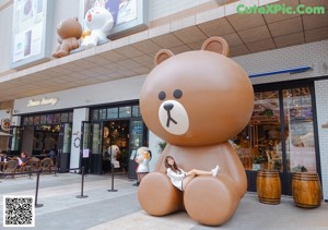 A woman posing with a large teddy bear in front of a store.