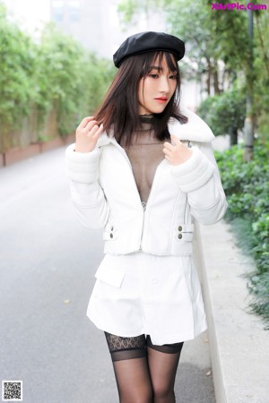 A woman in a white jacket and black hat is posing for a picture.