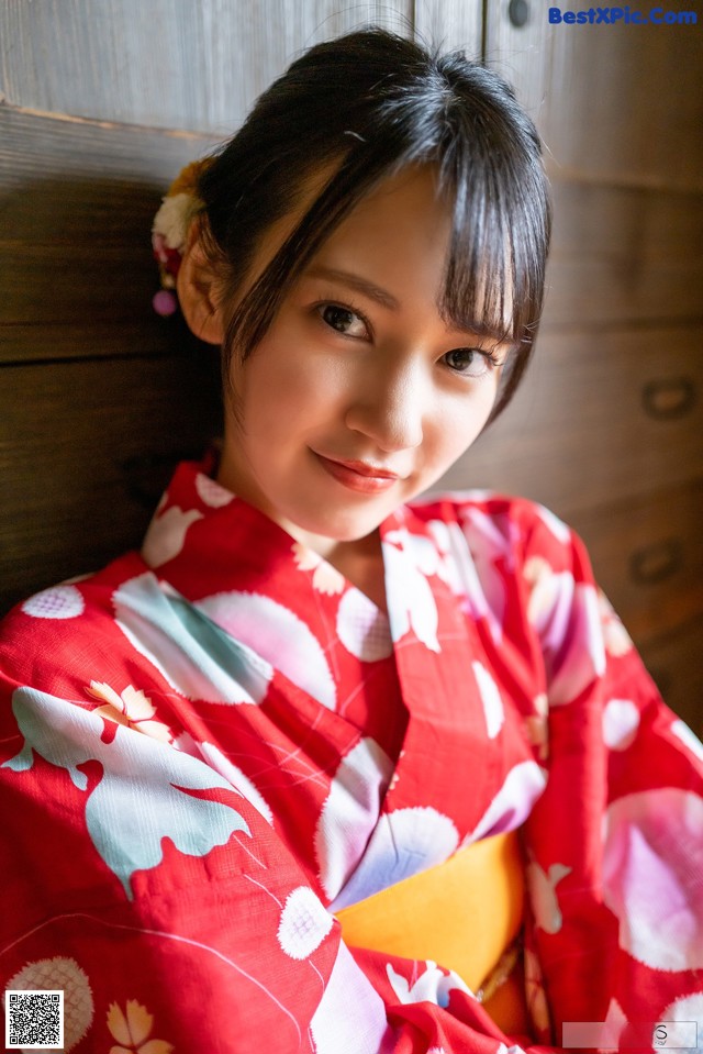 A woman in a red kimono sitting on a wooden bench.