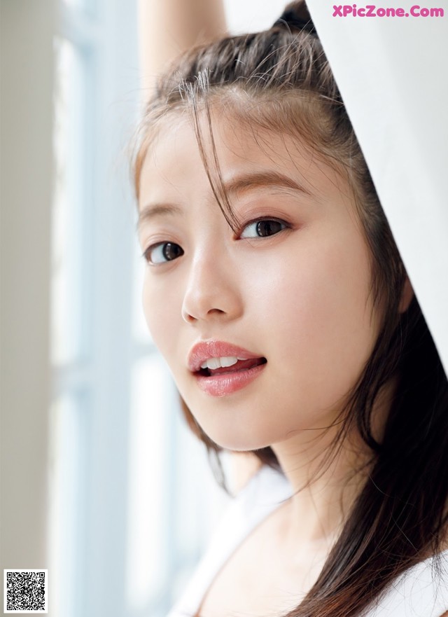 A woman with long brown hair leaning against a window.