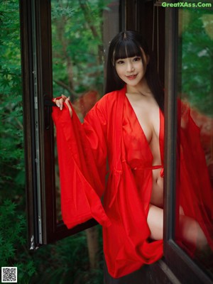 A woman in a red robe is looking out of a window.