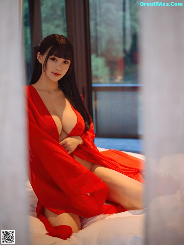 A woman in a red robe sitting on a bed.