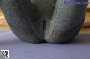 A woman in a white top and gray leggings is working out in a gym.