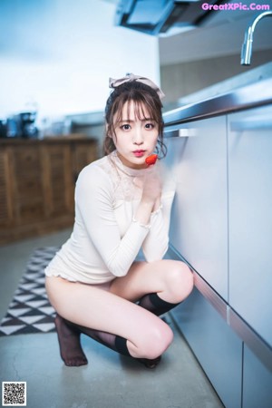 A woman sitting on top of a bed in a white sweater.