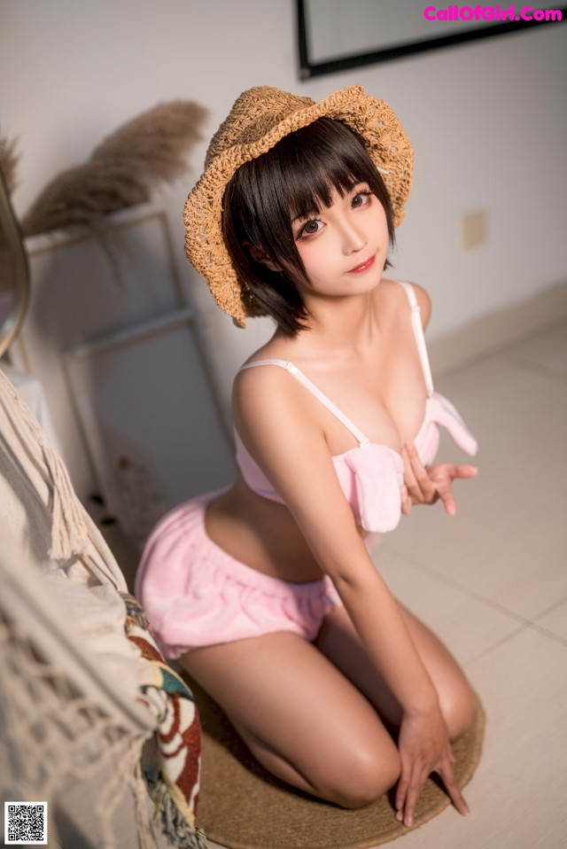 A woman in a pink bikini and a straw hat sitting on the floor.