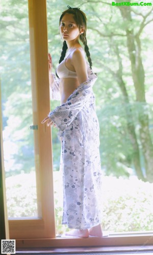 A woman in a white bikini standing in front of a window.