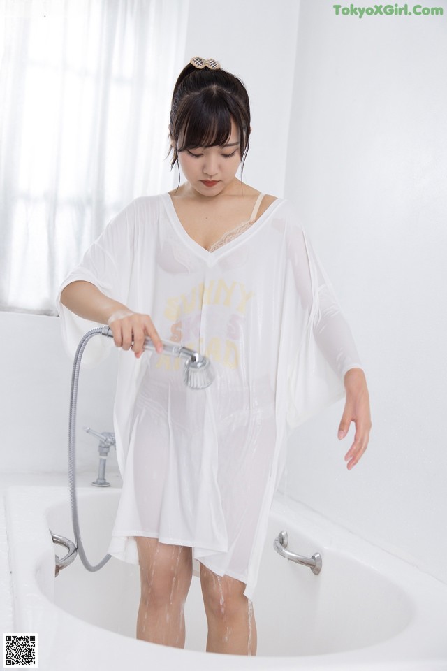 A woman standing in a bathtub holding a shower head.