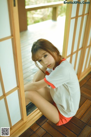 A woman sitting on a wooden floor next to a window.