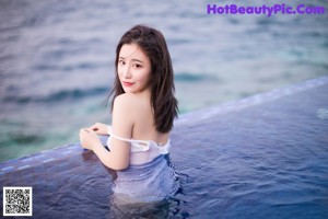 A woman in a white bathing suit sitting on a blue bench by the water.