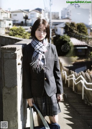 A woman in a school uniform leaning against a fence.