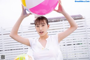 A woman in a white shirt and orange bikini playing with a beach ball.