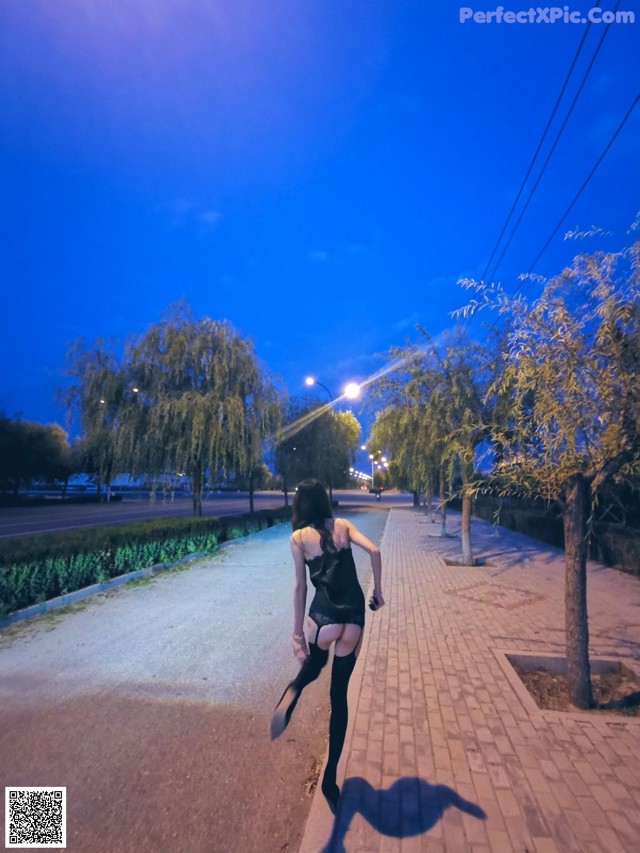 A woman in a black dress is walking down a sidewalk.