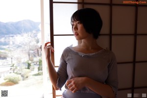 A naked asian woman sitting on a bed next to a window.