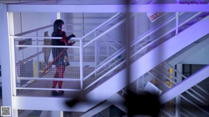 A woman in a black and red outfit holding a white mask.