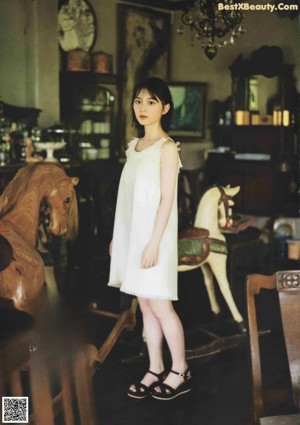 A woman in a white dress standing next to a rocking horse.