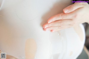 A woman in a white bodysuit and black stockings posing in a bathroom.